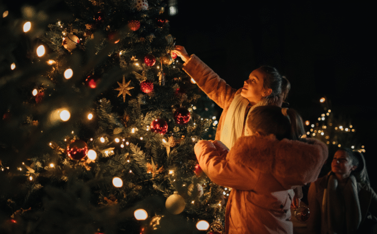 Family decorating a Christmas tree with lights and ornaments at an outdoor festive event – Christmas in Ireland 2025.