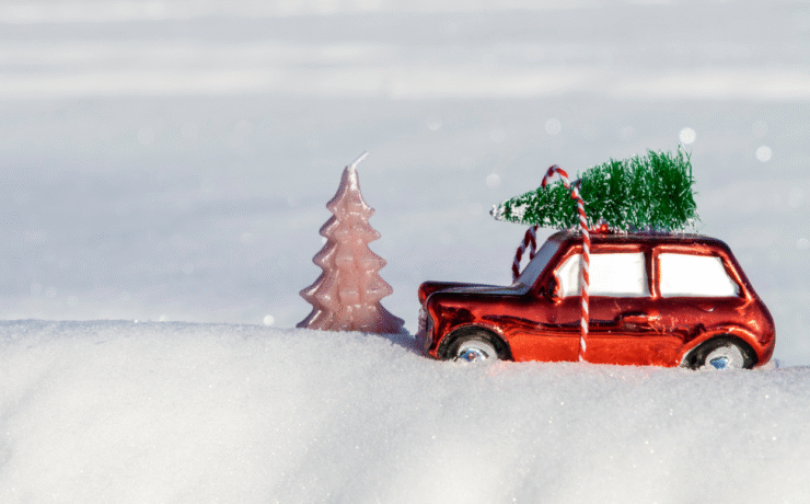 A small red car with a Christmas tree on the roof driving through snow, representing Easytrip’s free parking in Ireland offer during the festive season.