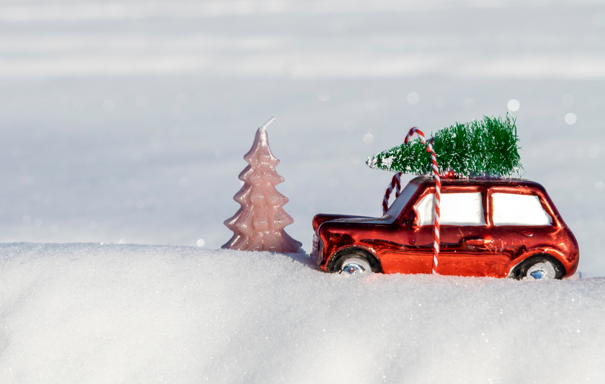A small red car with a Christmas tree on the roof driving through snow, representing Easytrip’s free parking in Ireland offer during the festive season.